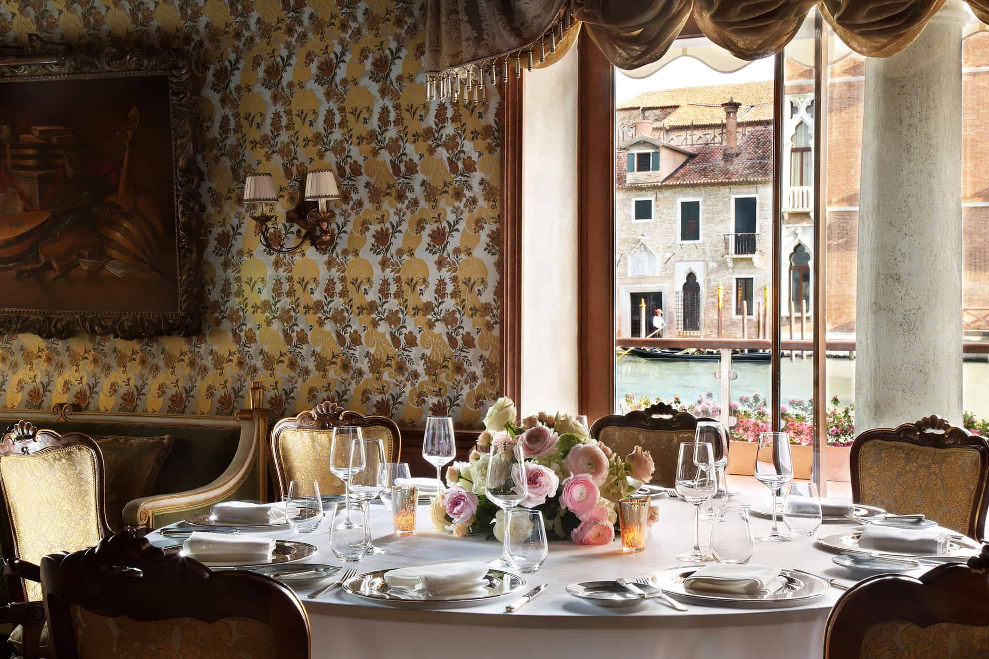 Mesa elegante dispuesta al estilo tradicional para seis junto a una ventana con vista a una góndola