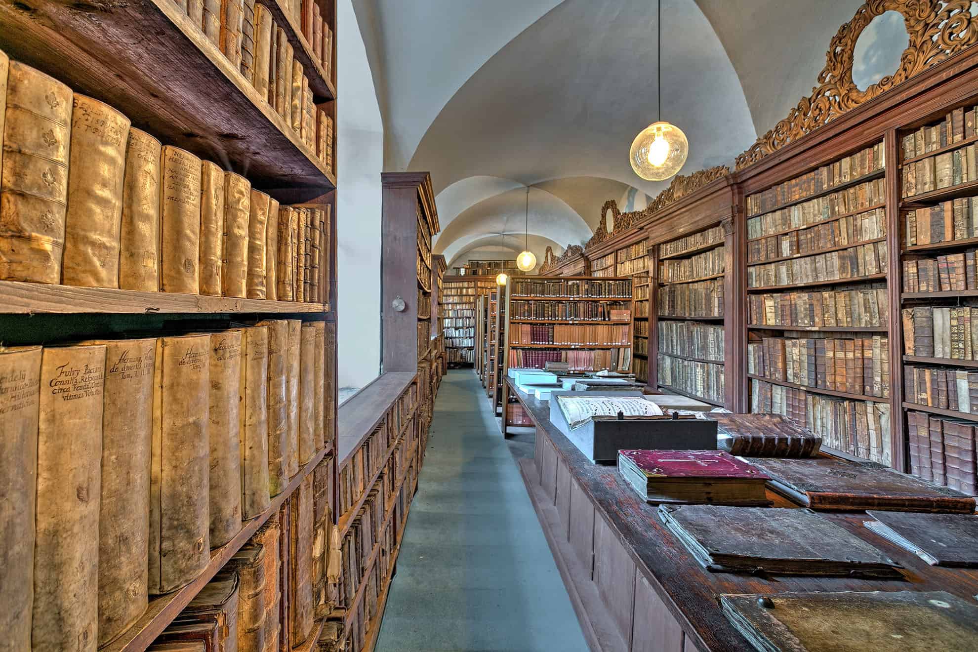Library filled with ornate shelves of antique books and long table filled with large books
