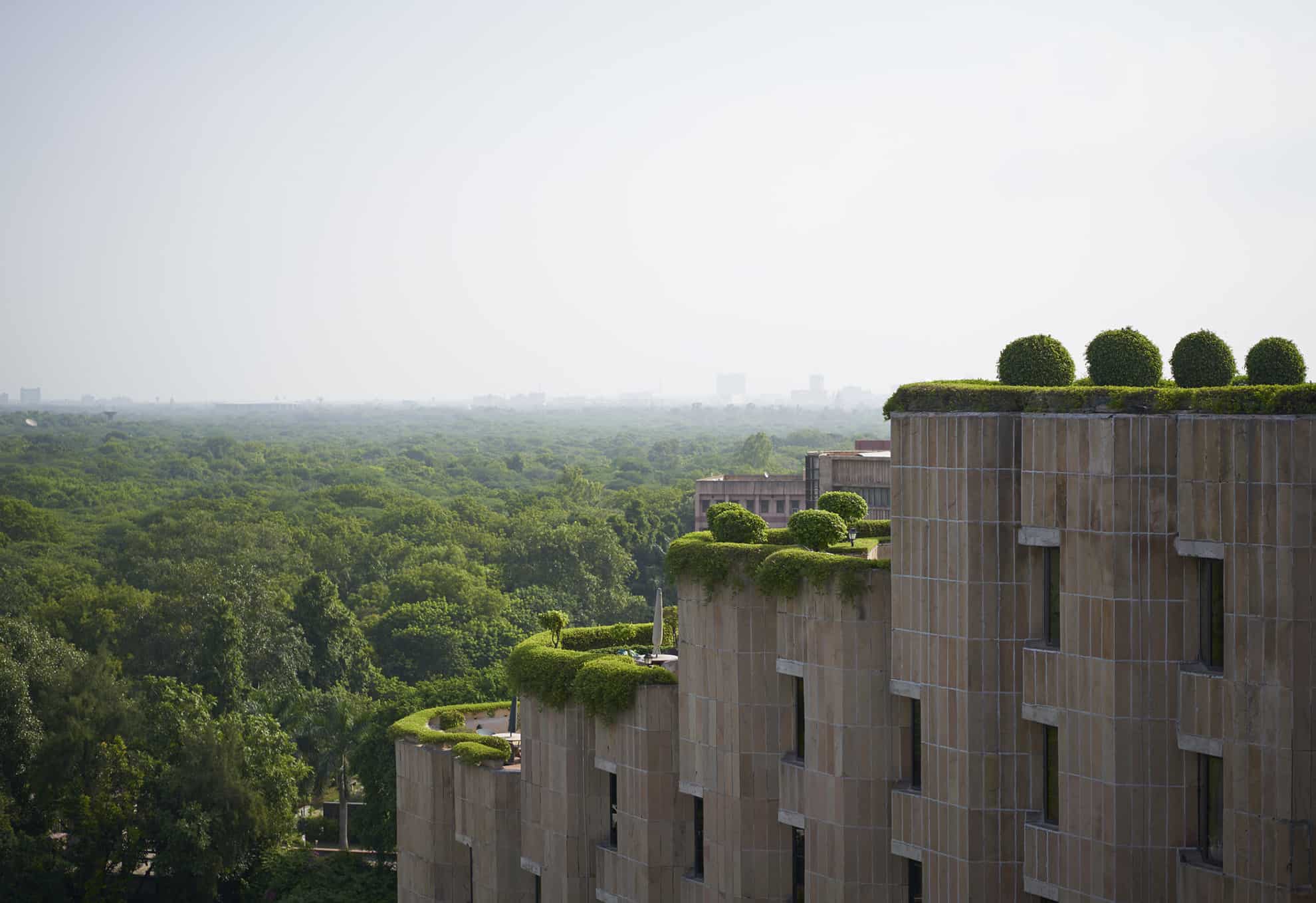 Large stone building with 4 tiered levels of rooftop garden terraces overlooking tree-covered land