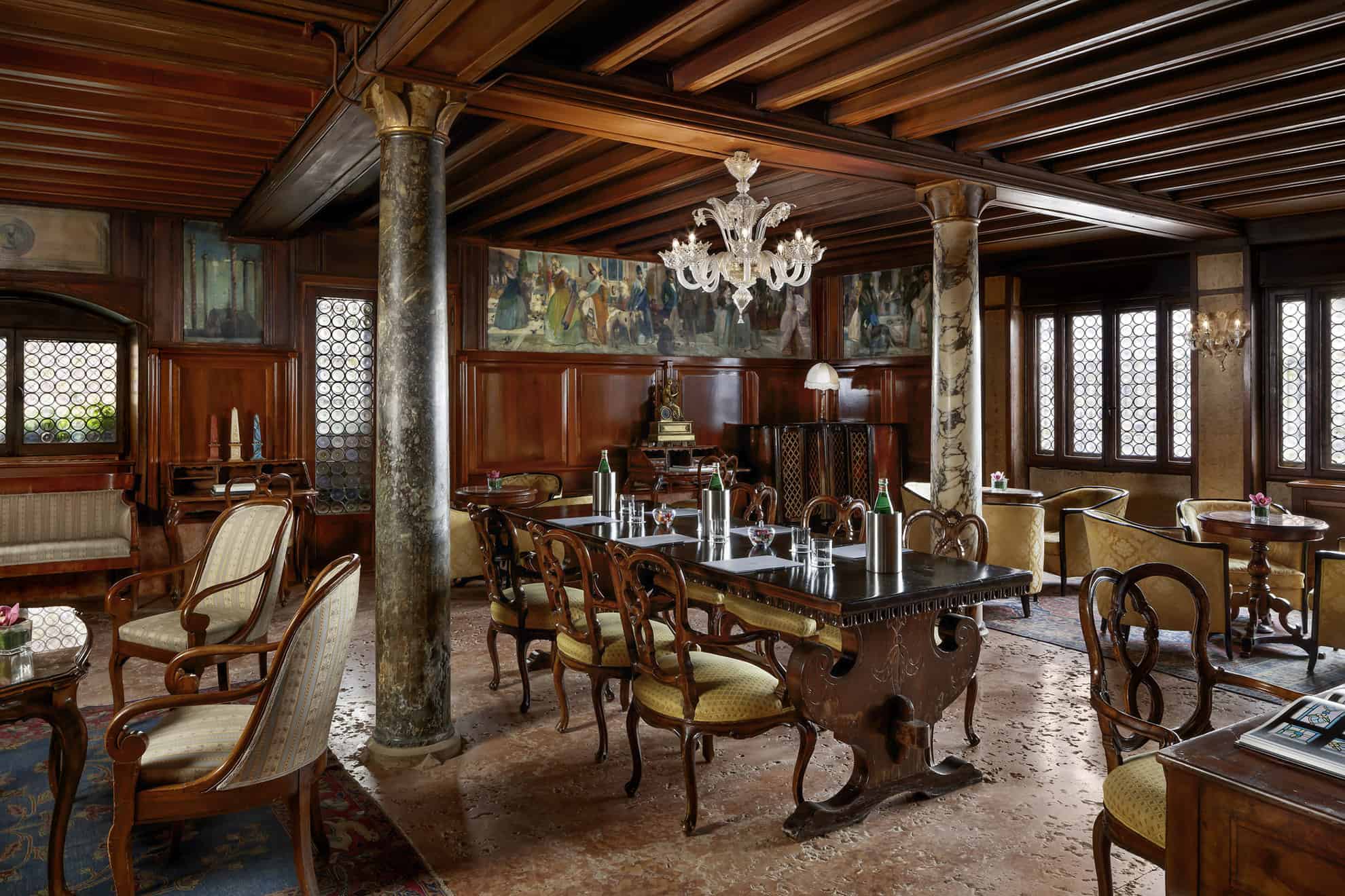 Salón con paneles de madera y columnas de mármol, una mesa lista y otros juegos de mesa pequeños