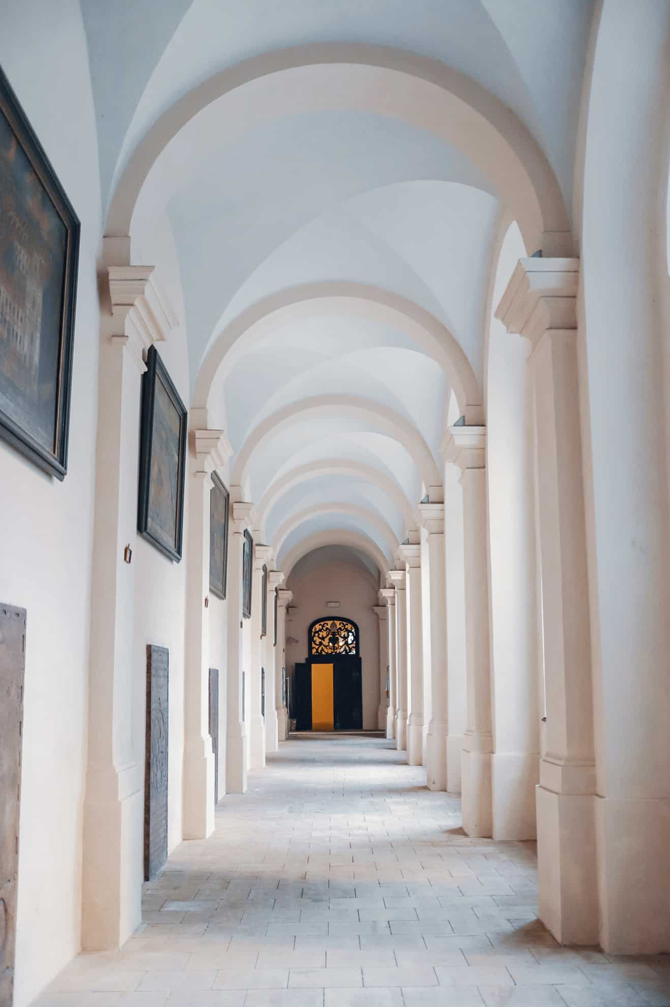 Long white hall with arched ceiling and dark door at end