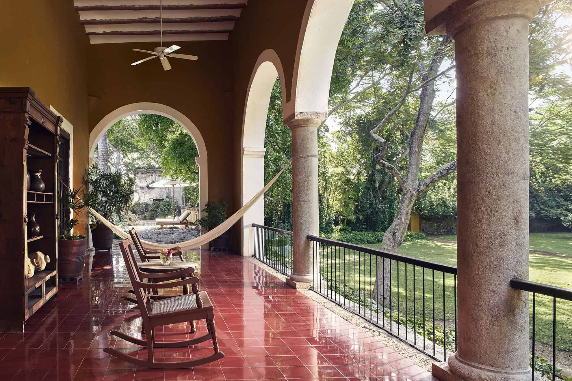 Red-tiled porch with pillared archways, large hammock, and wooden rocking chairs with side table