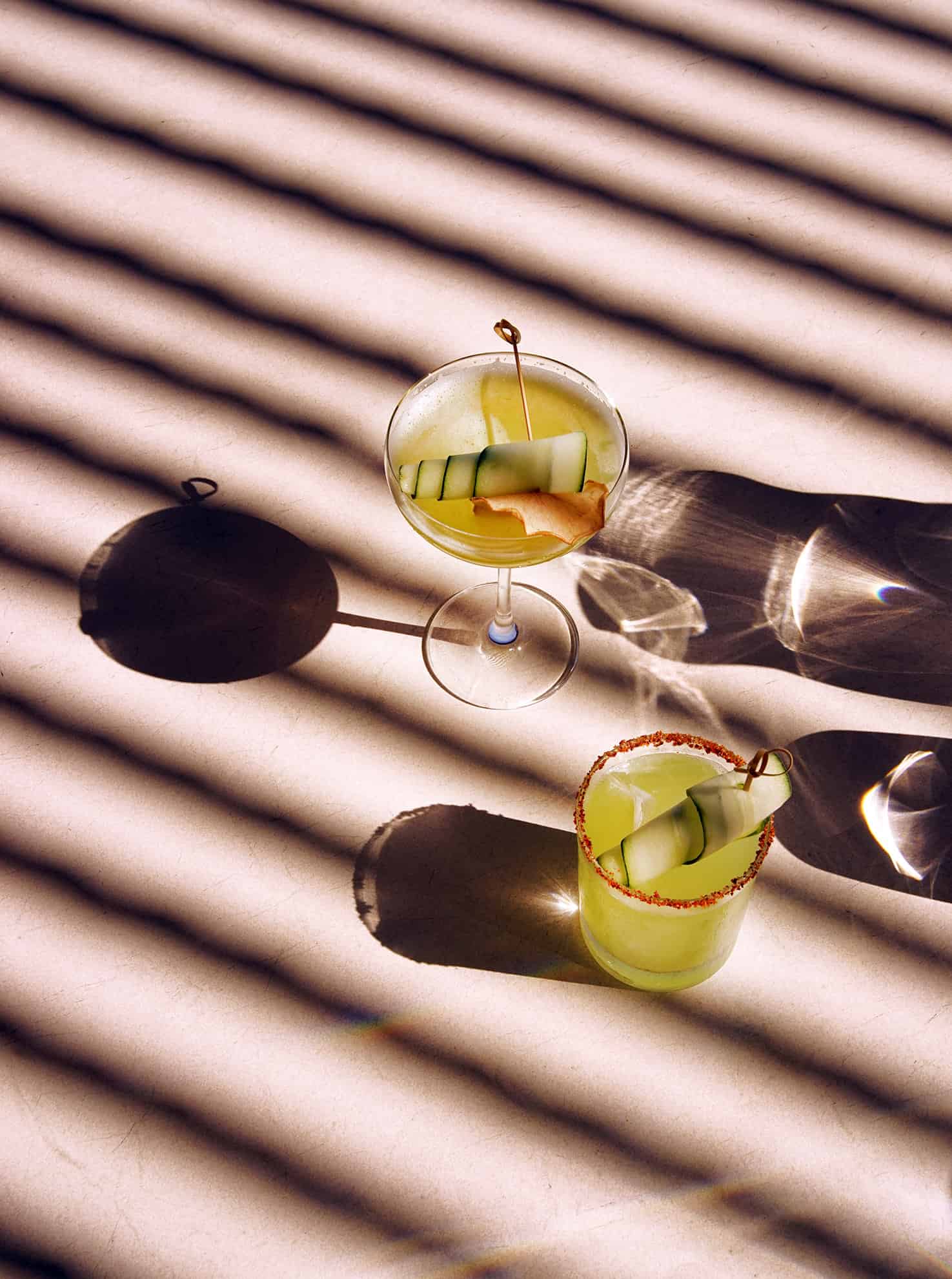 Martini and rocks glasses filled with custom cocktails garnished with cucumber