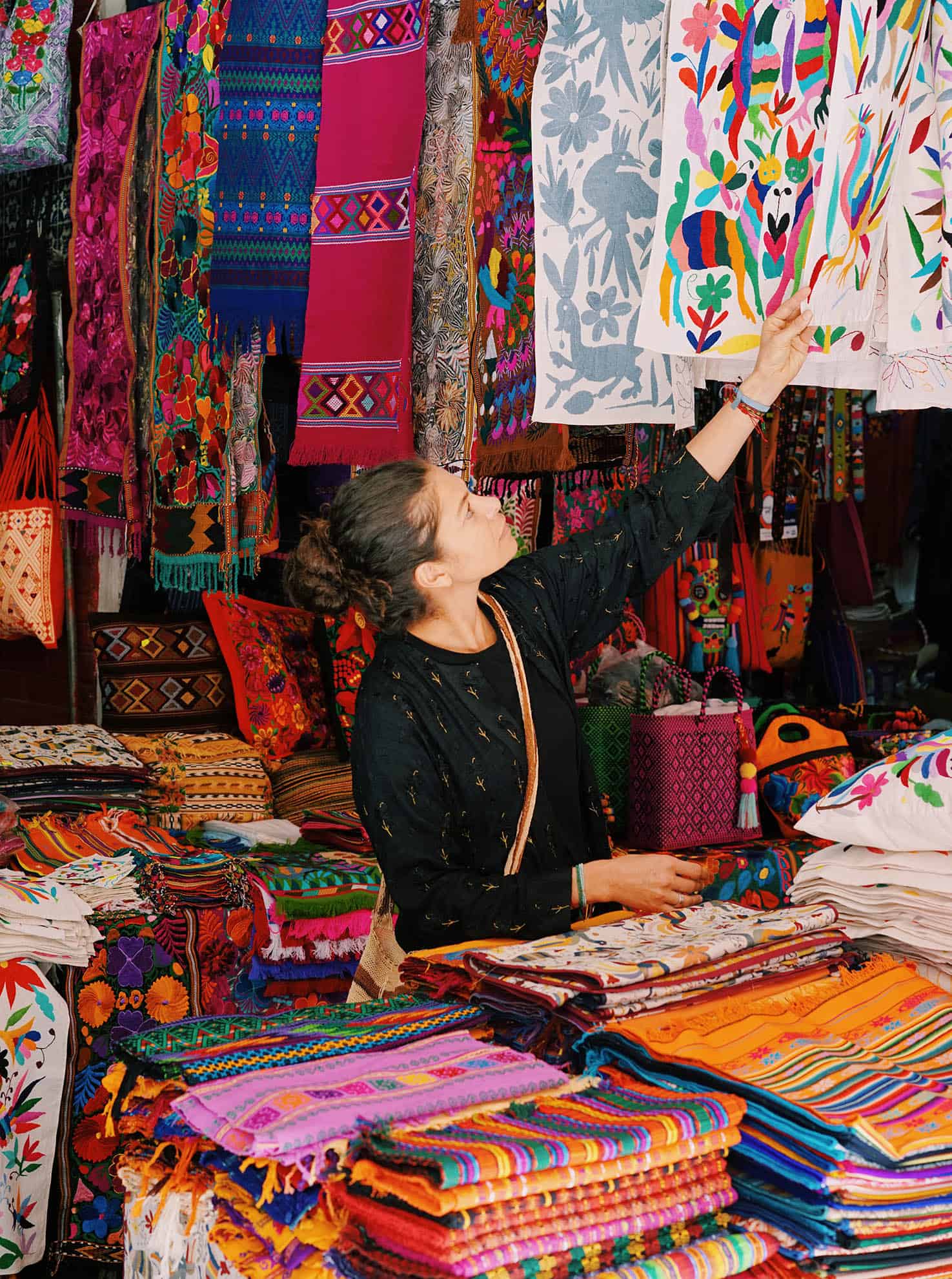 Woman in a local shop looking through colorful fabrics; arm reaching up grabbing a patterned fabric
