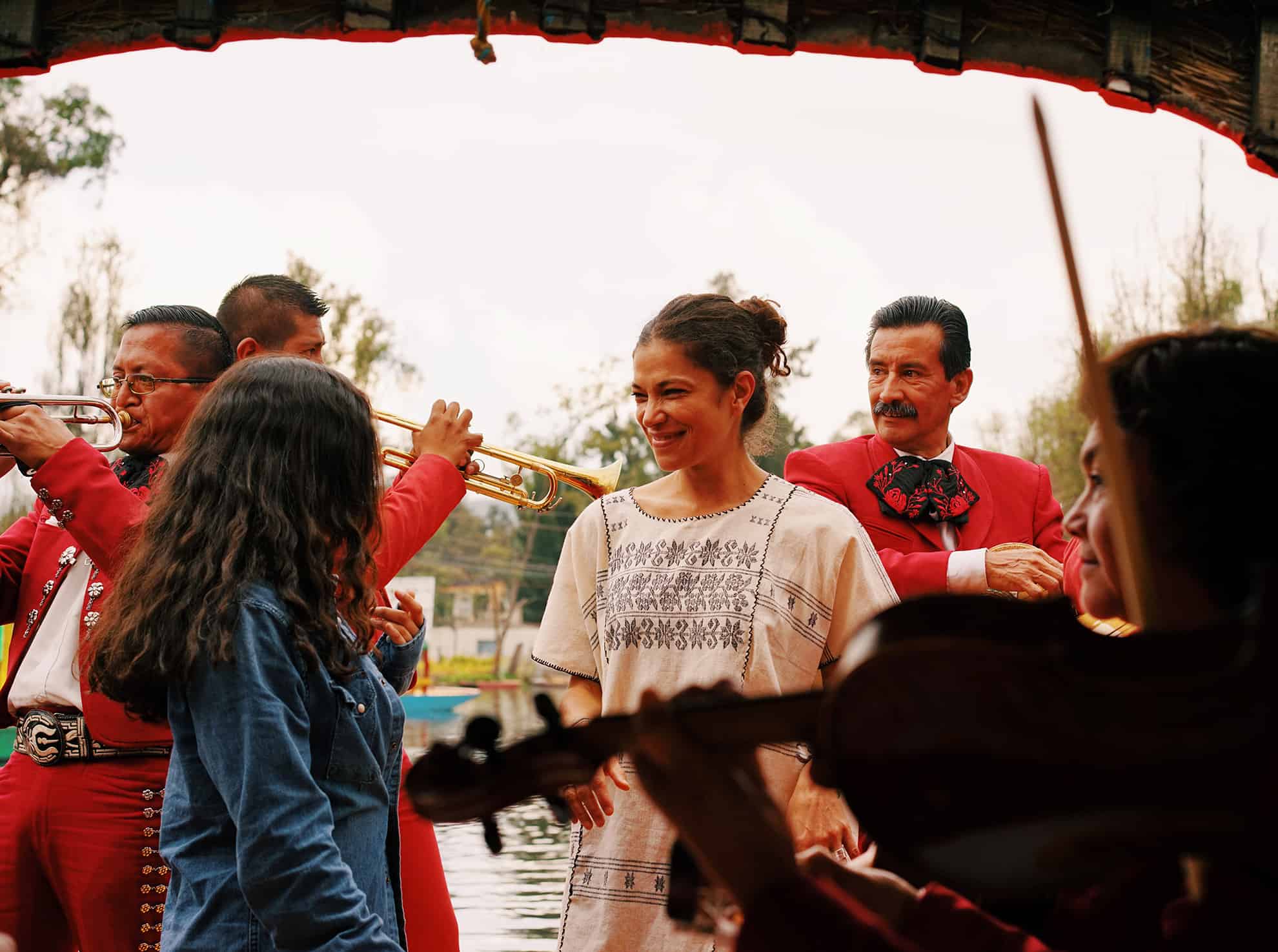 Two women smiling & talking surrounded by Mariachi band members playing instruments