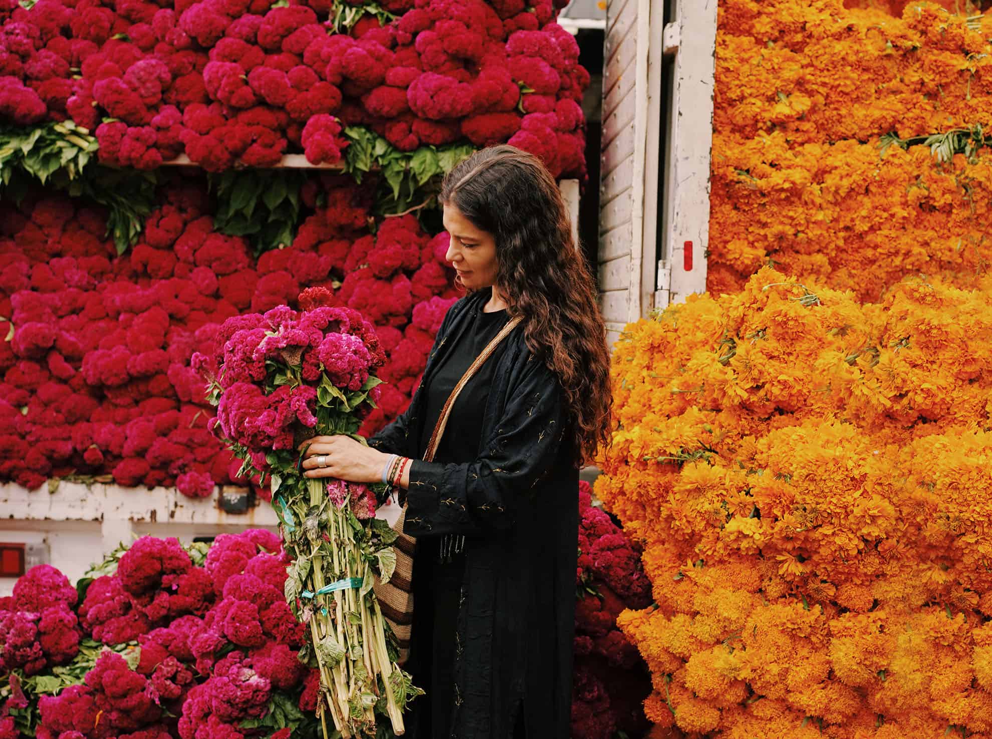 Woman holding bouquet of flowers at a floral shop in front of a wall of bright blooms