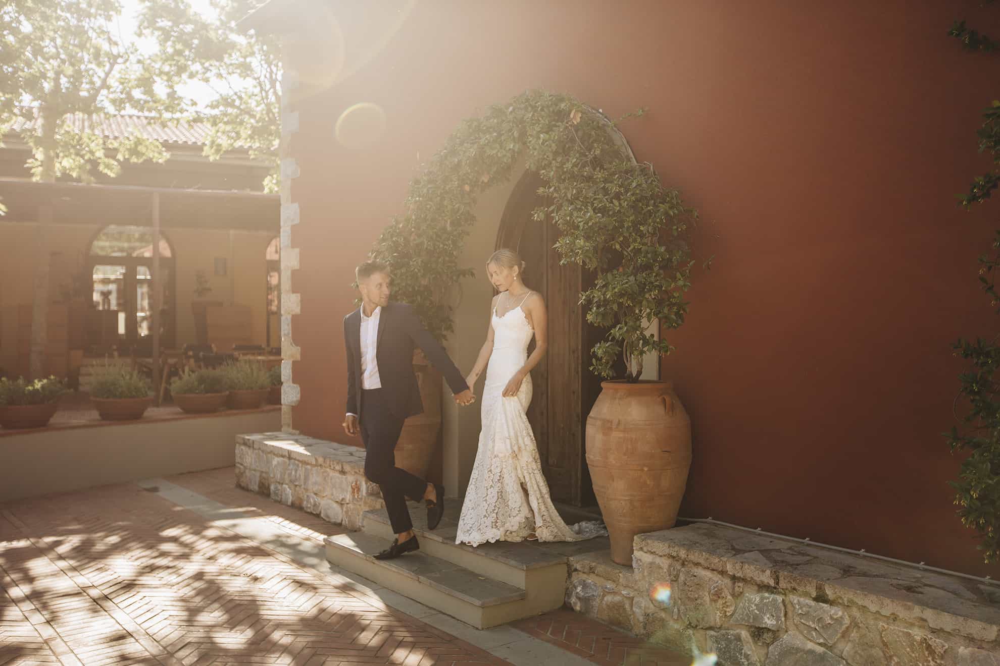 Pareja de recién casados saliendo de una capilla con un arco de flores; el novio mira a la novia