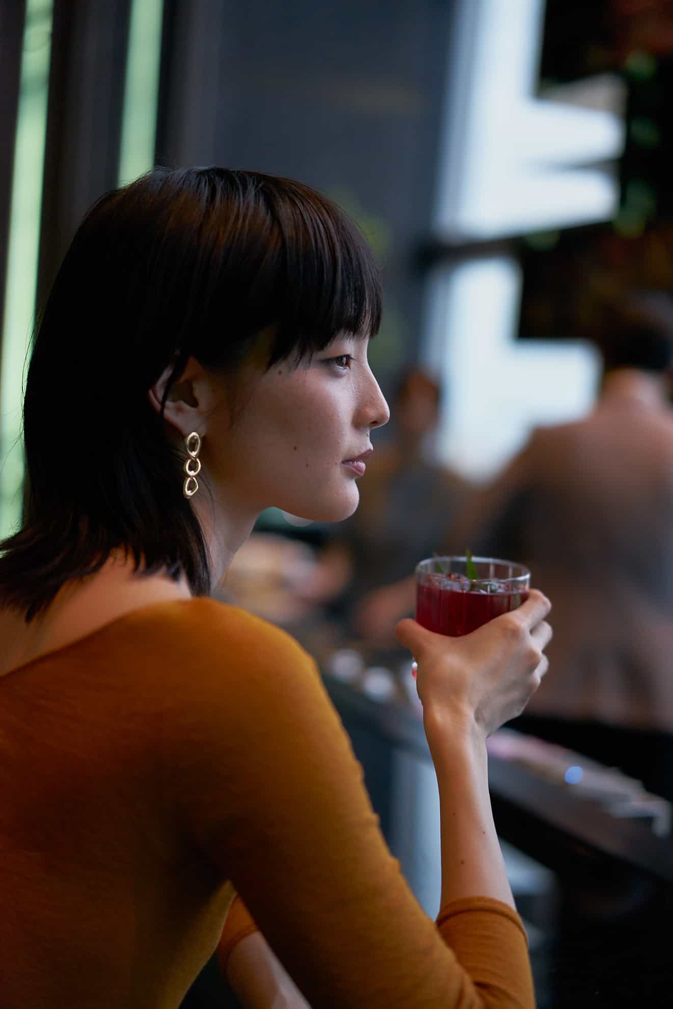Profile of stylish young woman holding a cocktail and leaning on a bar
