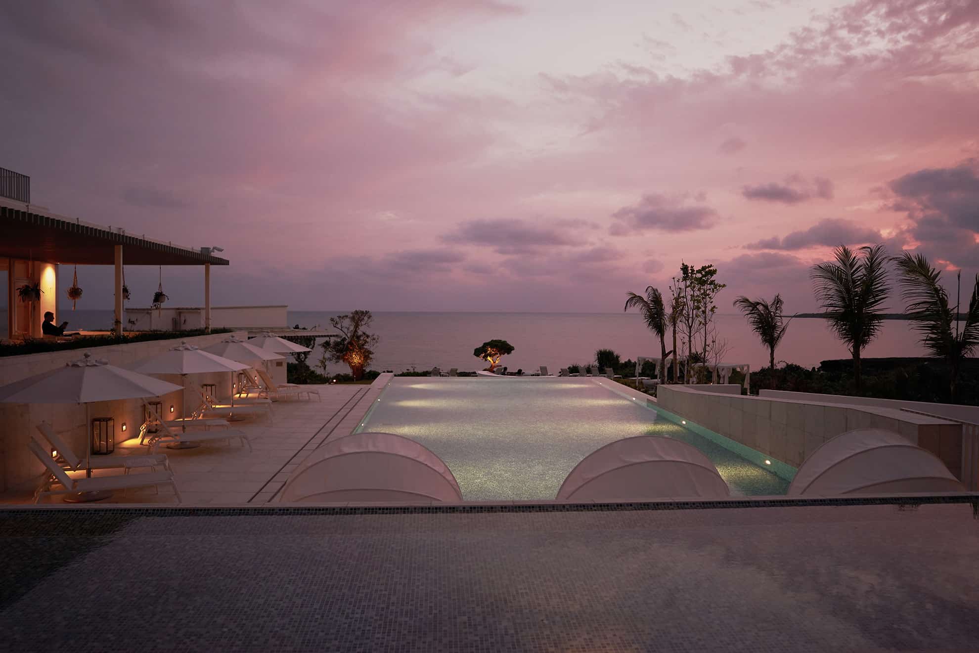Infinity pool with ocean view lined with loungers and umbrellas at dusk