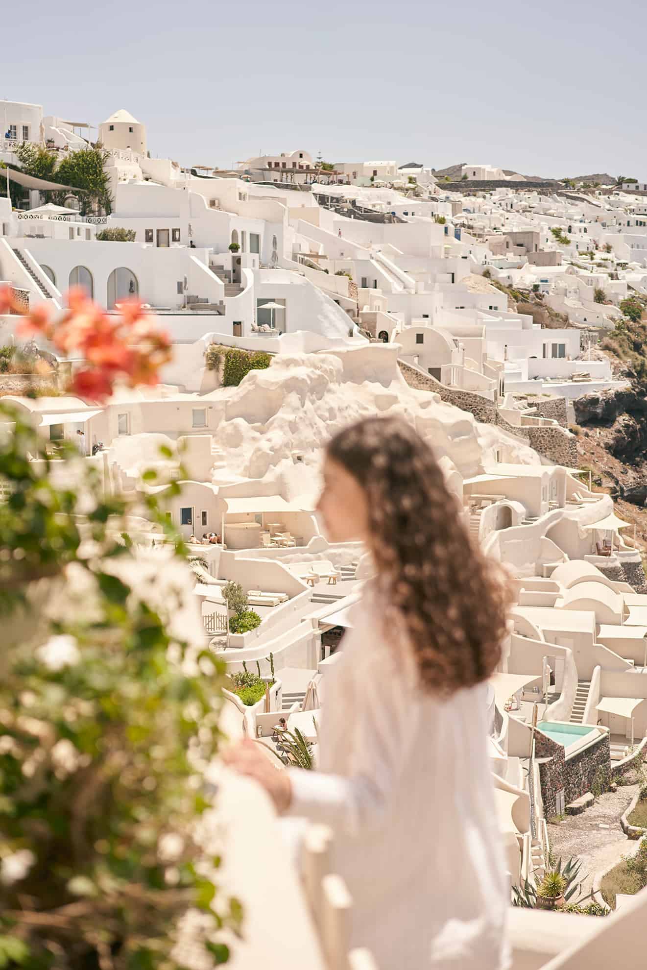 Blurry side view of woman in foreground with clear view of white city on hill in background.