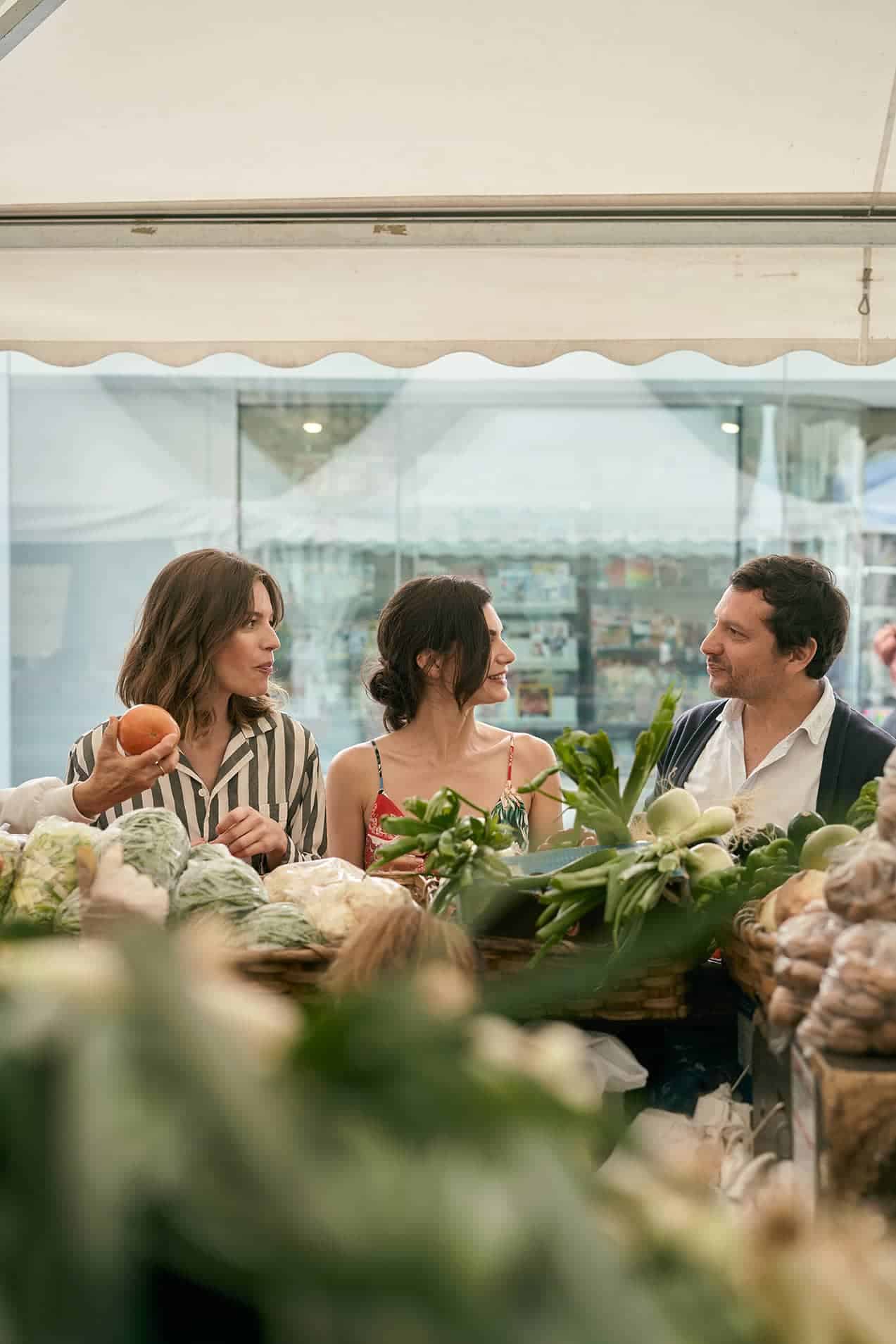 Drei Personen im Gespräch, die sich Gemüse auf einem Händlermarkt im Freien anschauen