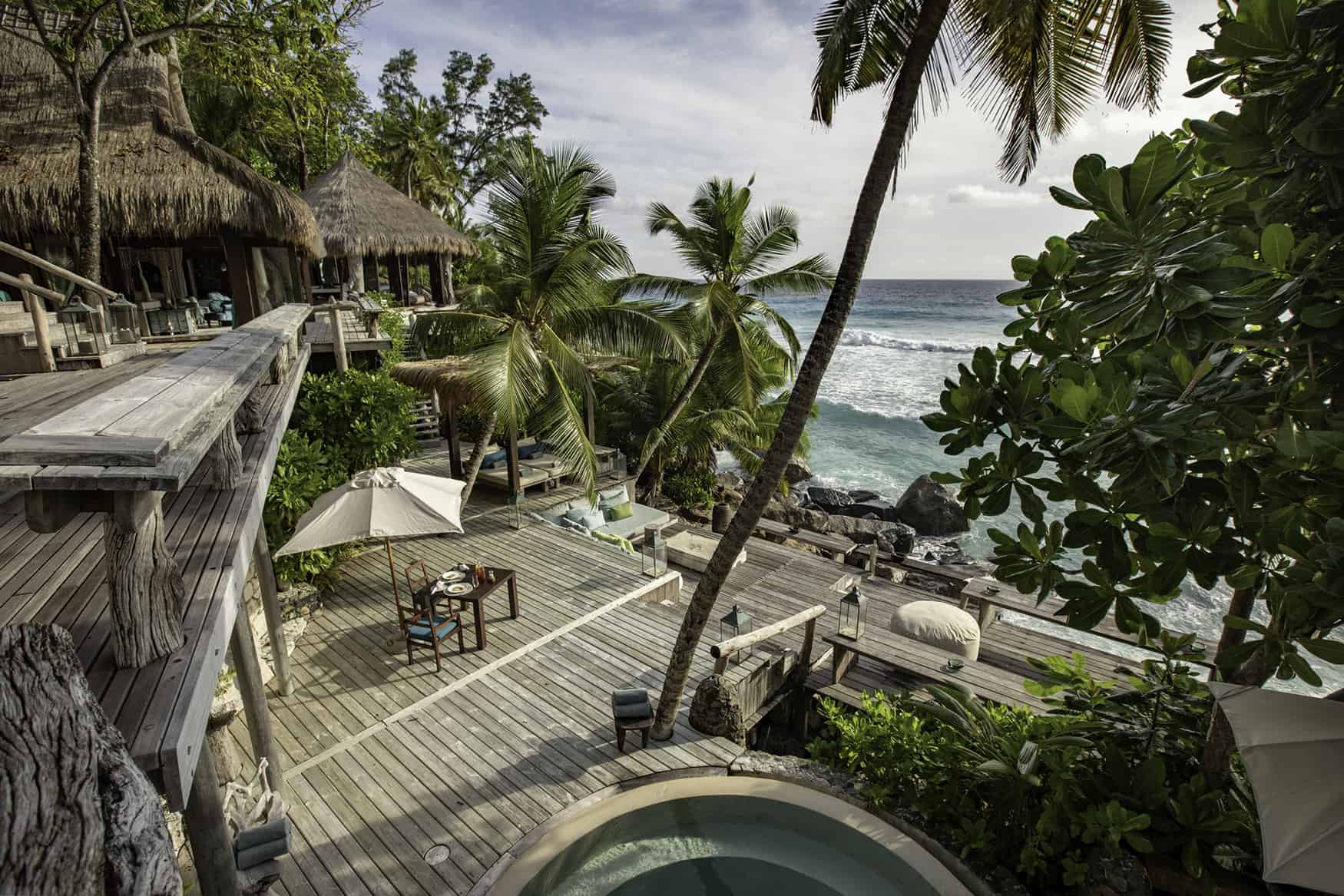 Aerial view of multi-level patio with various seating, tropical landscaping and waves rolling in