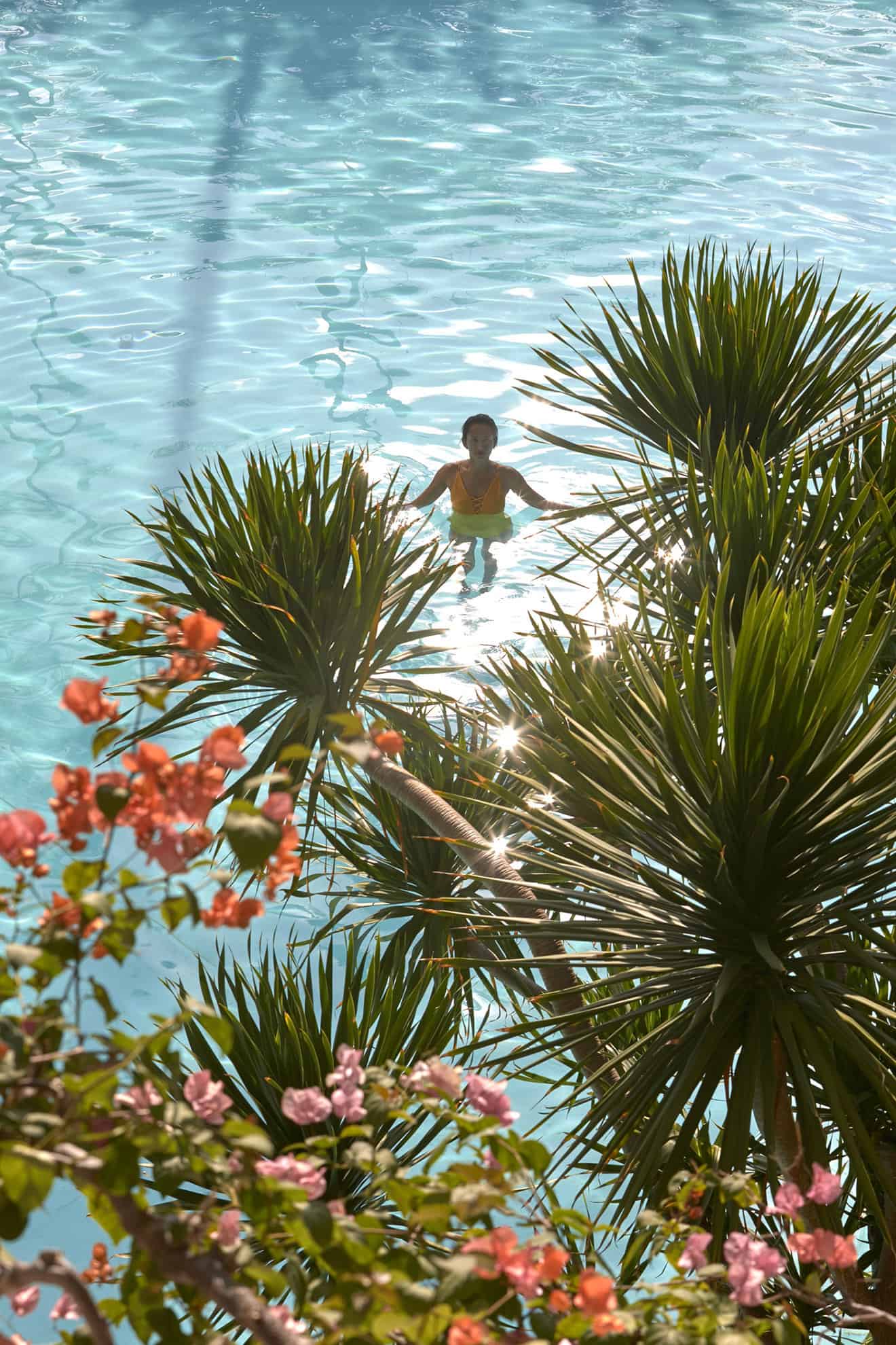 Vista de cima de mulher de pé em piscina através de galhos de árvore tropical florida