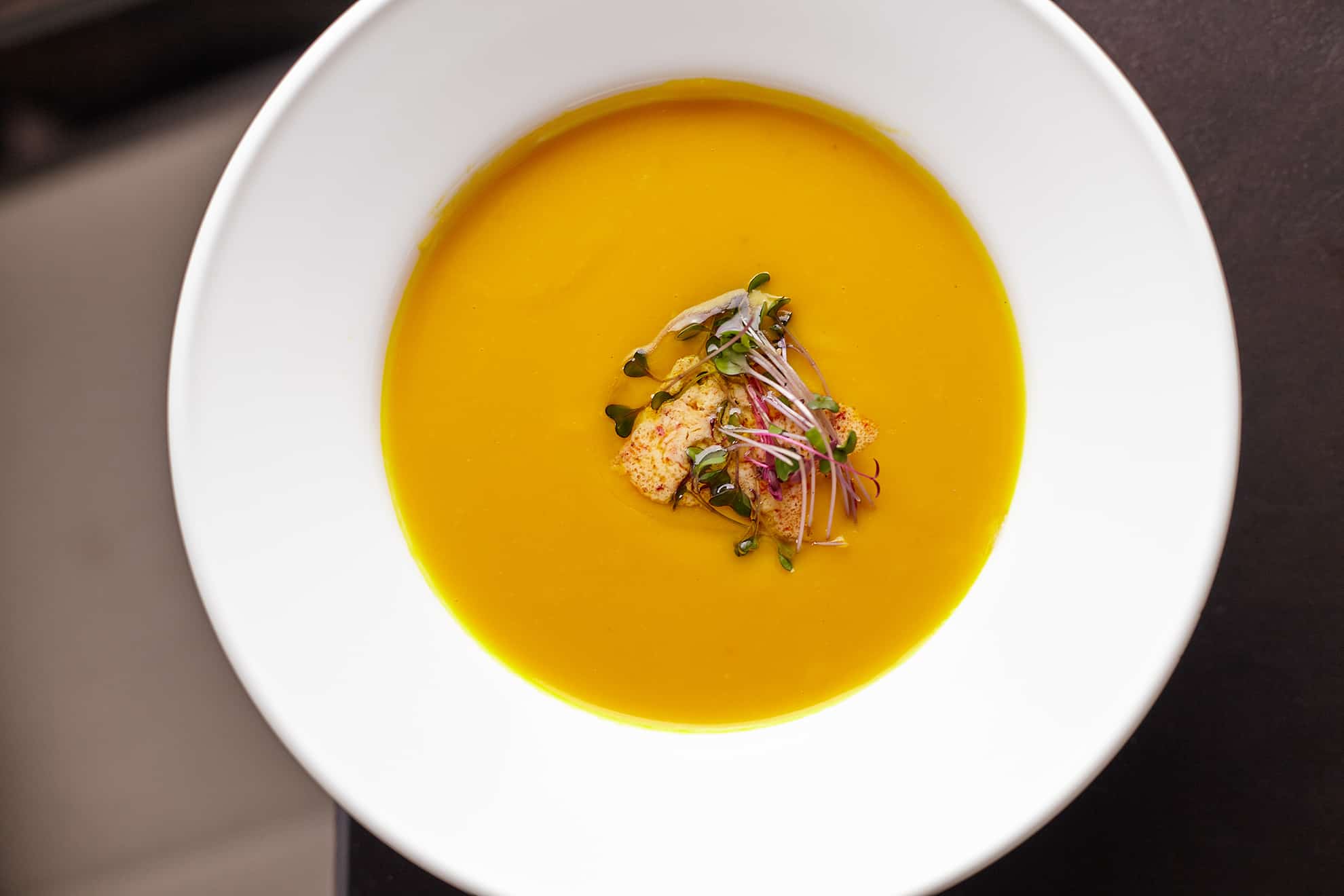 Nahaufnahme einer Schüssel mit orangefarbener Suppe mit Brot und Garnierung