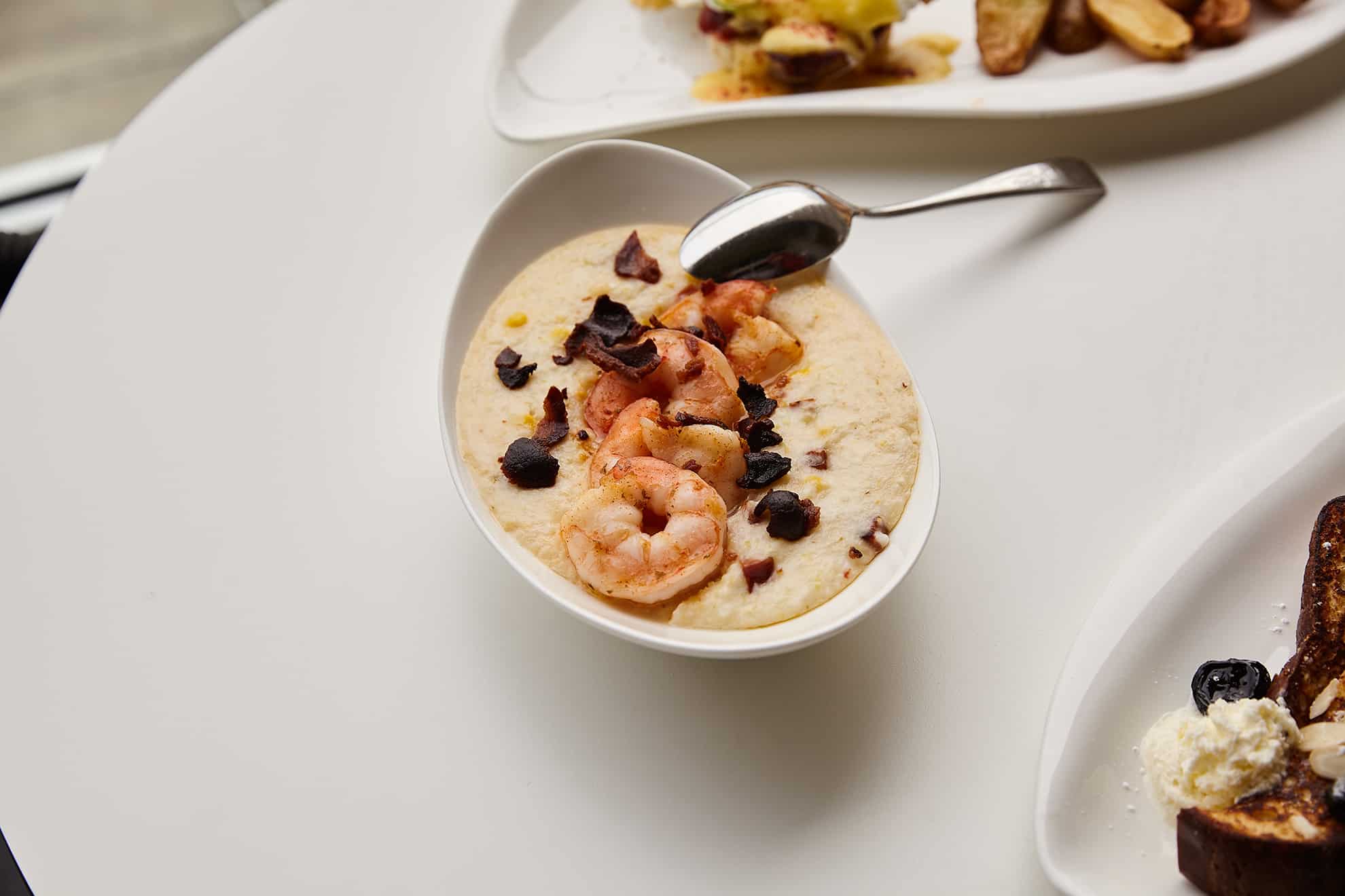 Shrimp dish with spoon atop a table with two other dishes nearby