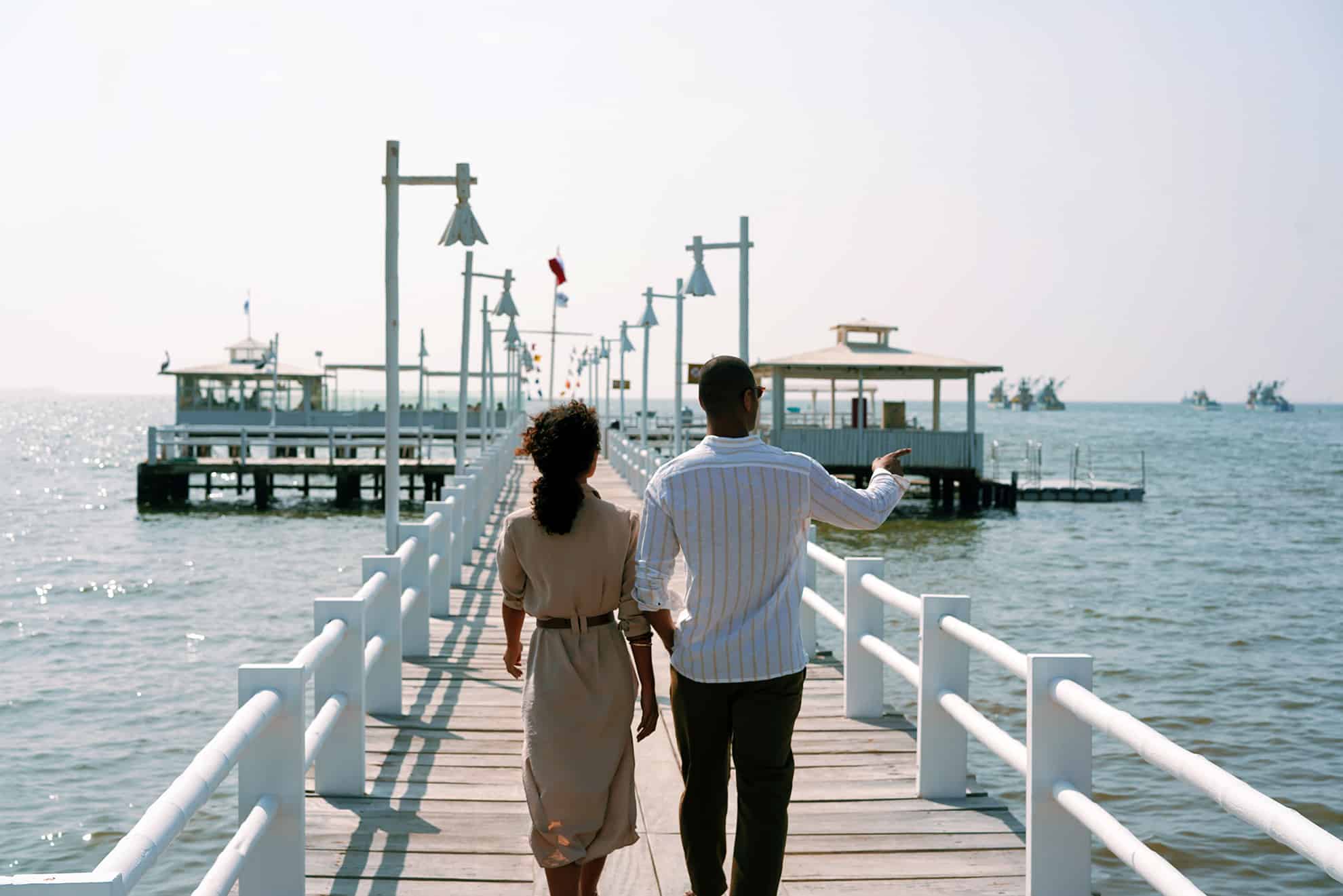 Back view of a couple walking on a pier toward dock on the ocean admiring the surroundings