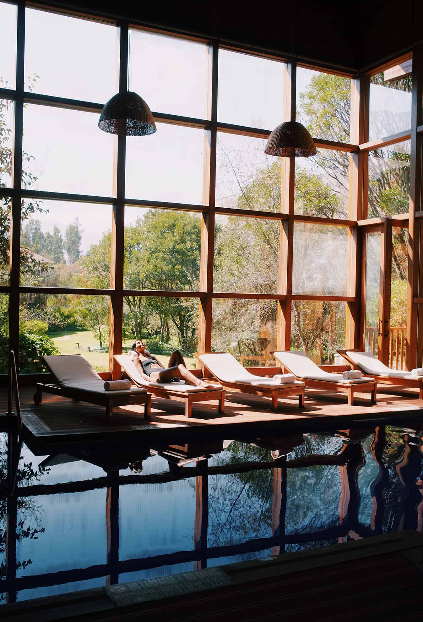 Mujer una silla junto a la piscina con ventanas del piso al techo y vista a la naturaleza