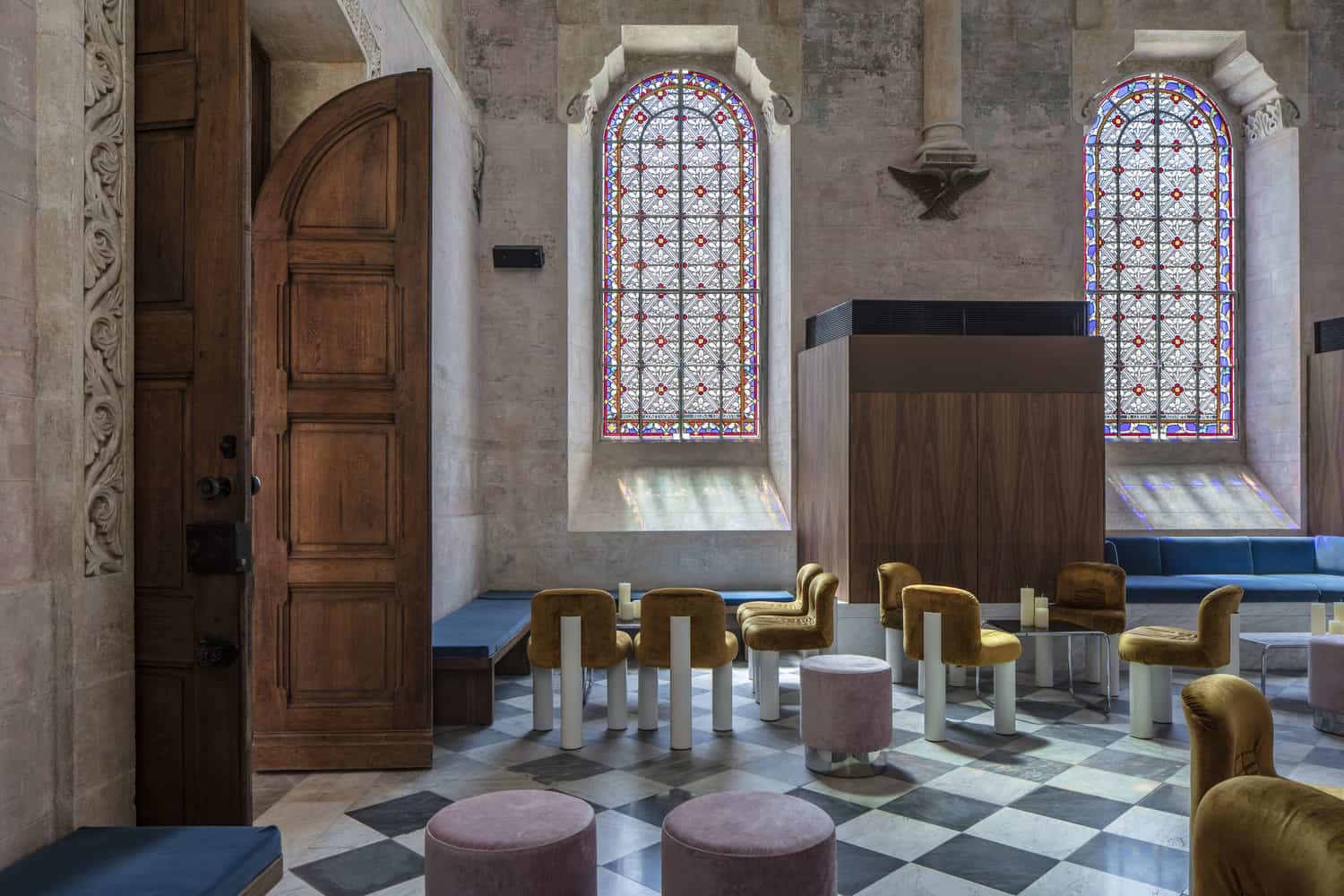 Sala de capilla con piso de baldosas, dos ventanas en forma de arco y vitral y sillas de terciopelo
