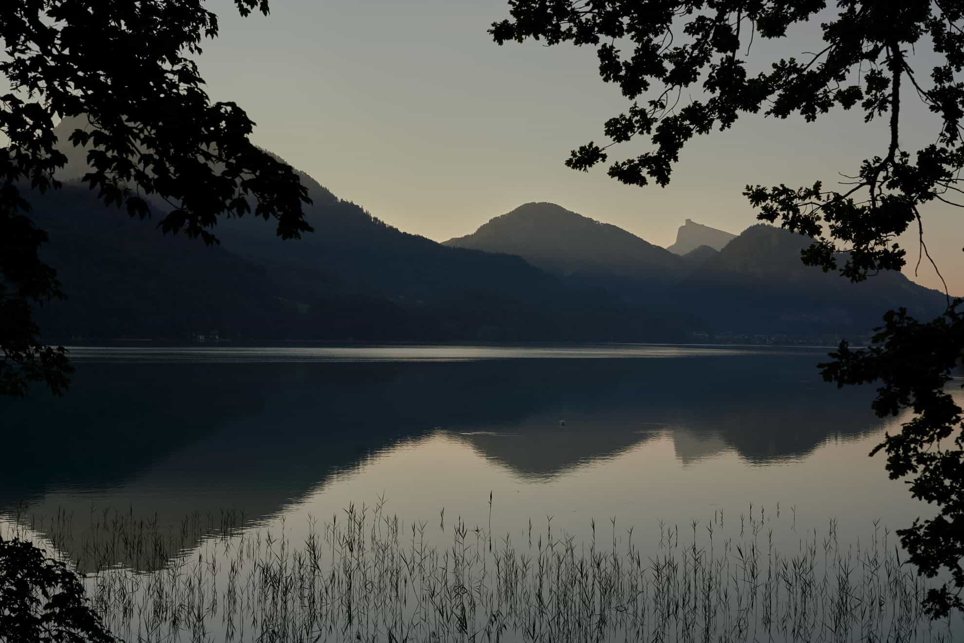 Serene lake with tree-covered hills reflecting on the water at dusk
