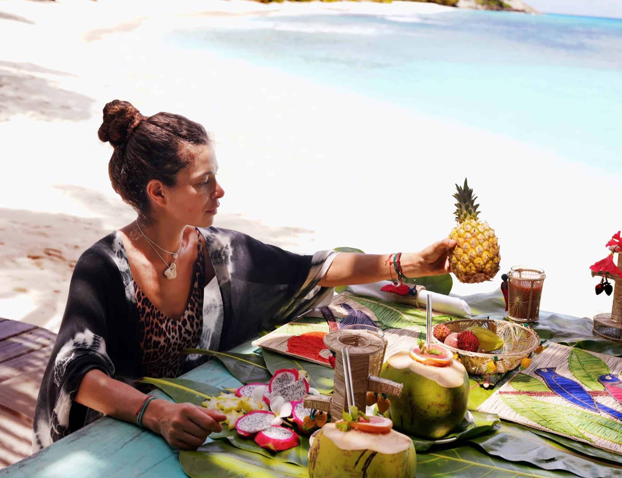 woman on beach sitting at table filled with fruits