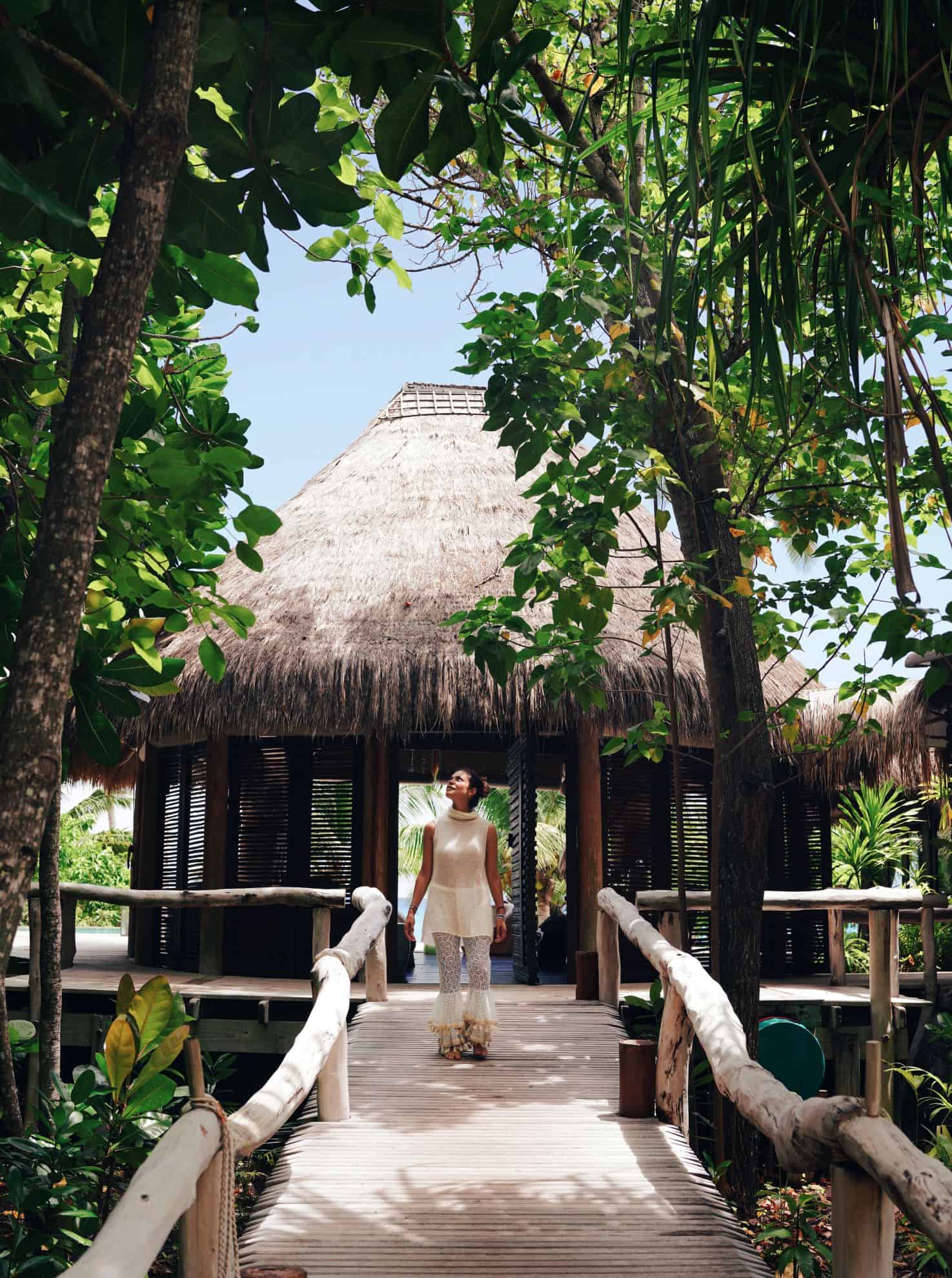 Woman standing on wooden walkway in front of hut with thatched roof