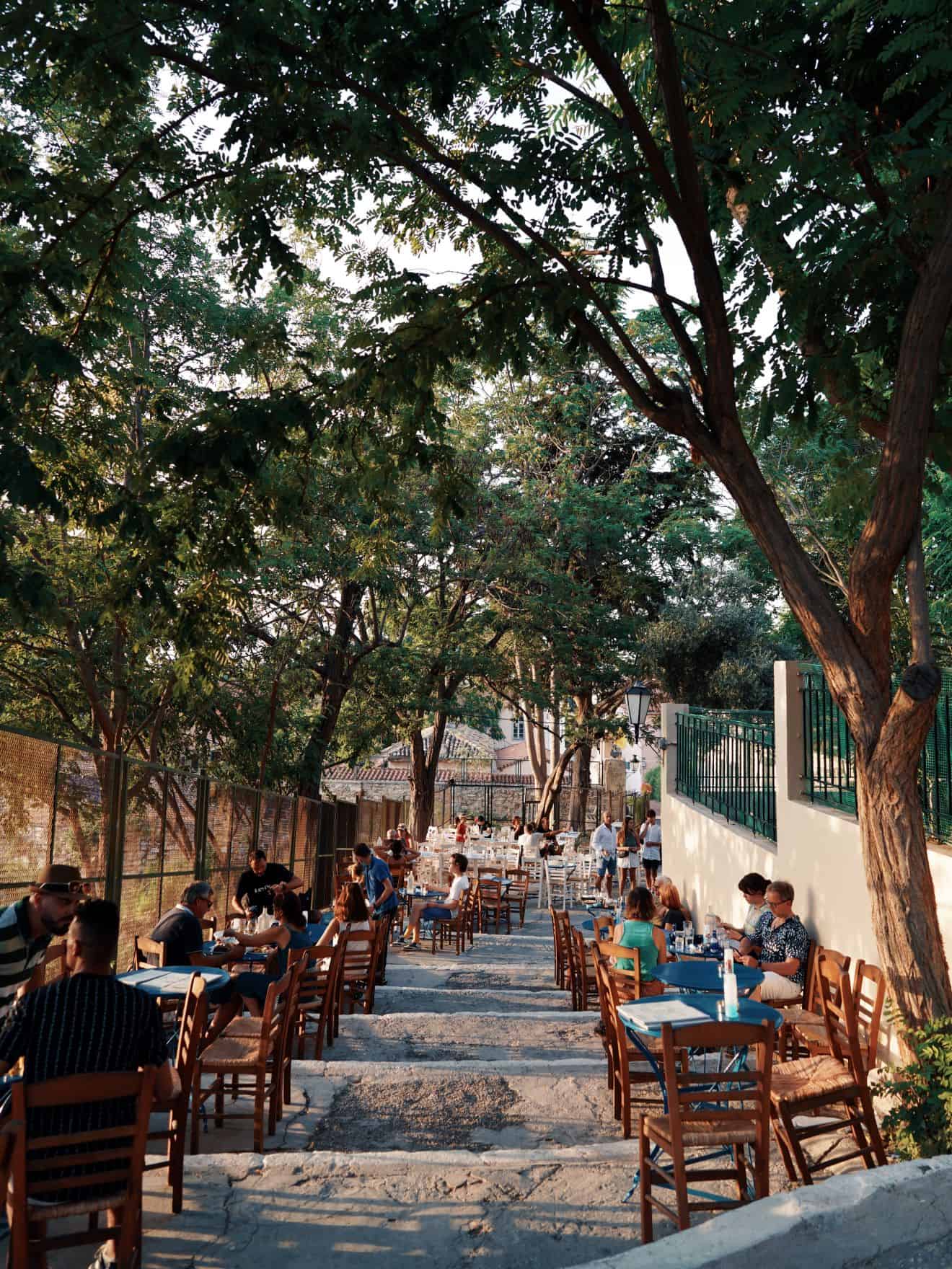 Outdoor dining area with tables and chairs on pathway shaded by trees