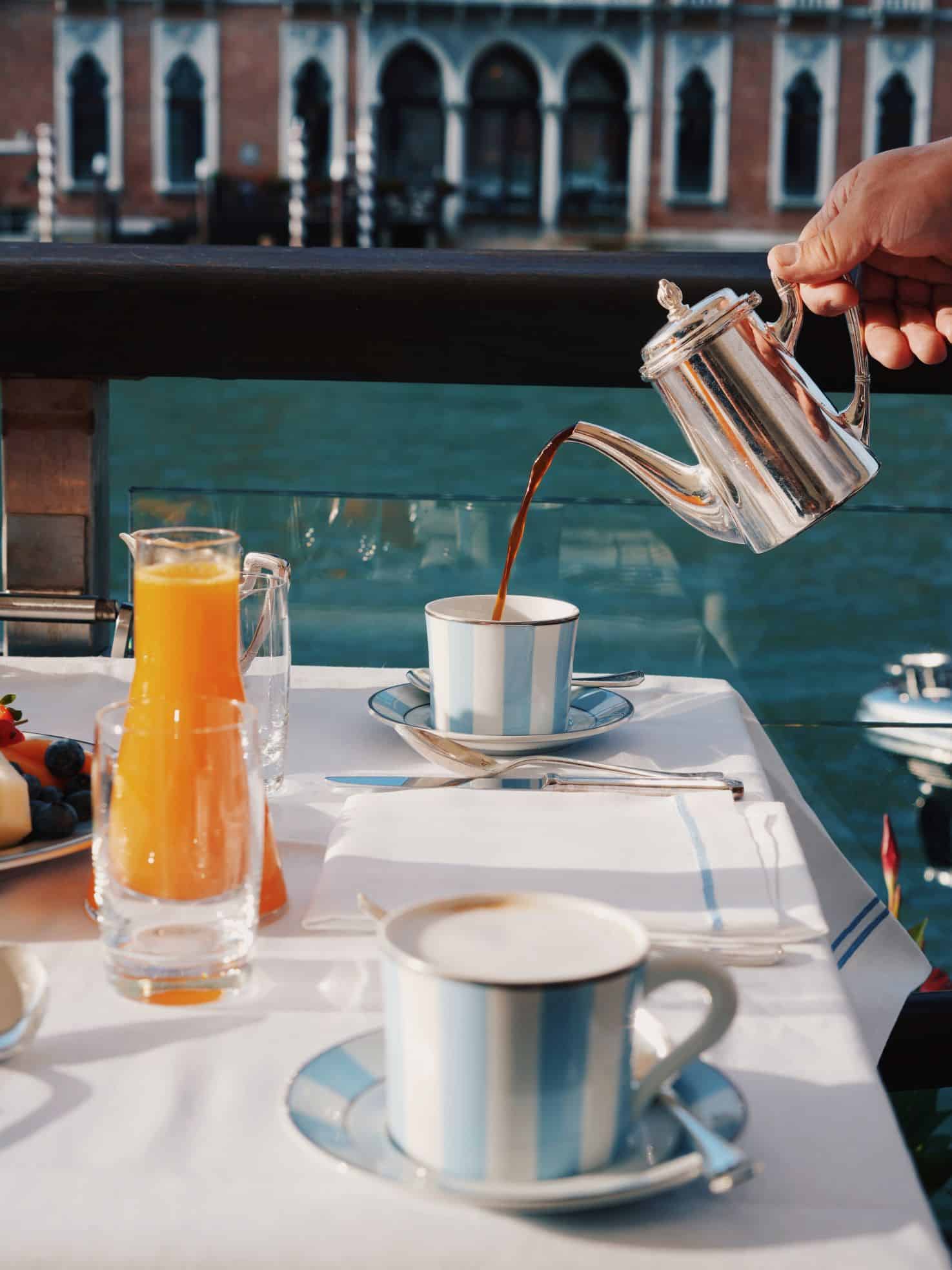 Table with carafe of orange juice and tea being poured from silver pot into teacup