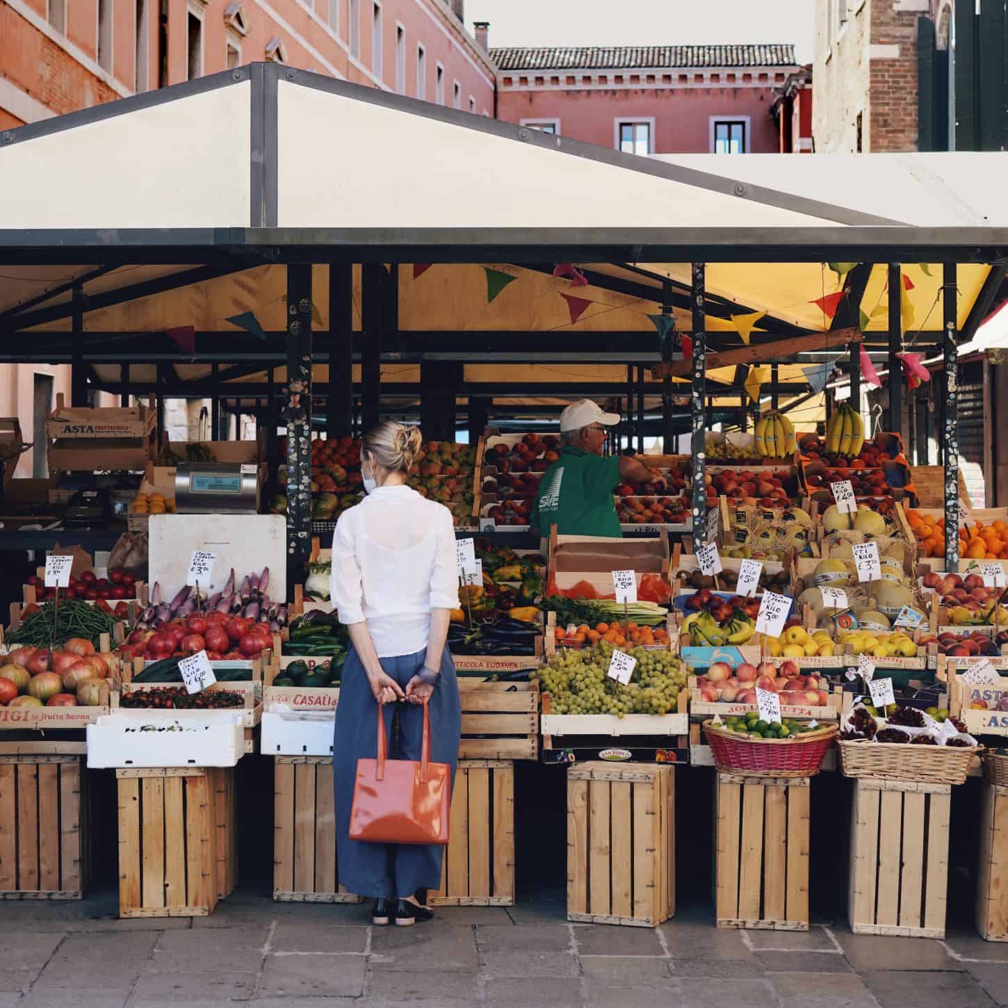 Woman in front of outdoor market stand filled with fruit and produce