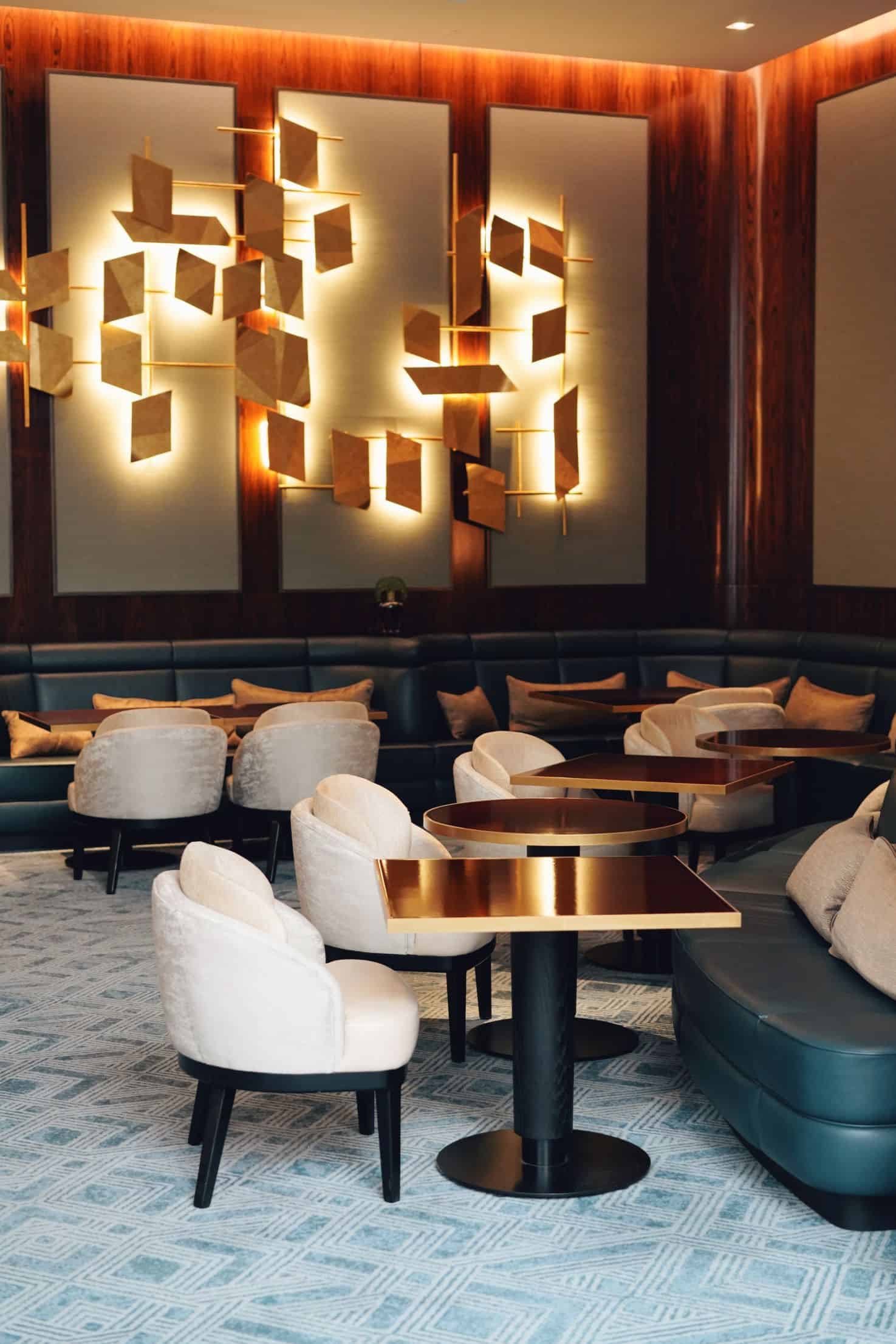 Dimly lit restaurant with booths, upholstered chairs, and modern geometric chandelier