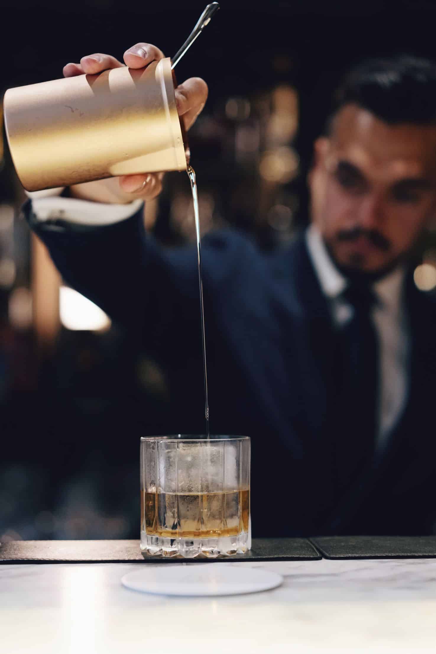 Man in suite pouring cocktail from gold decanter