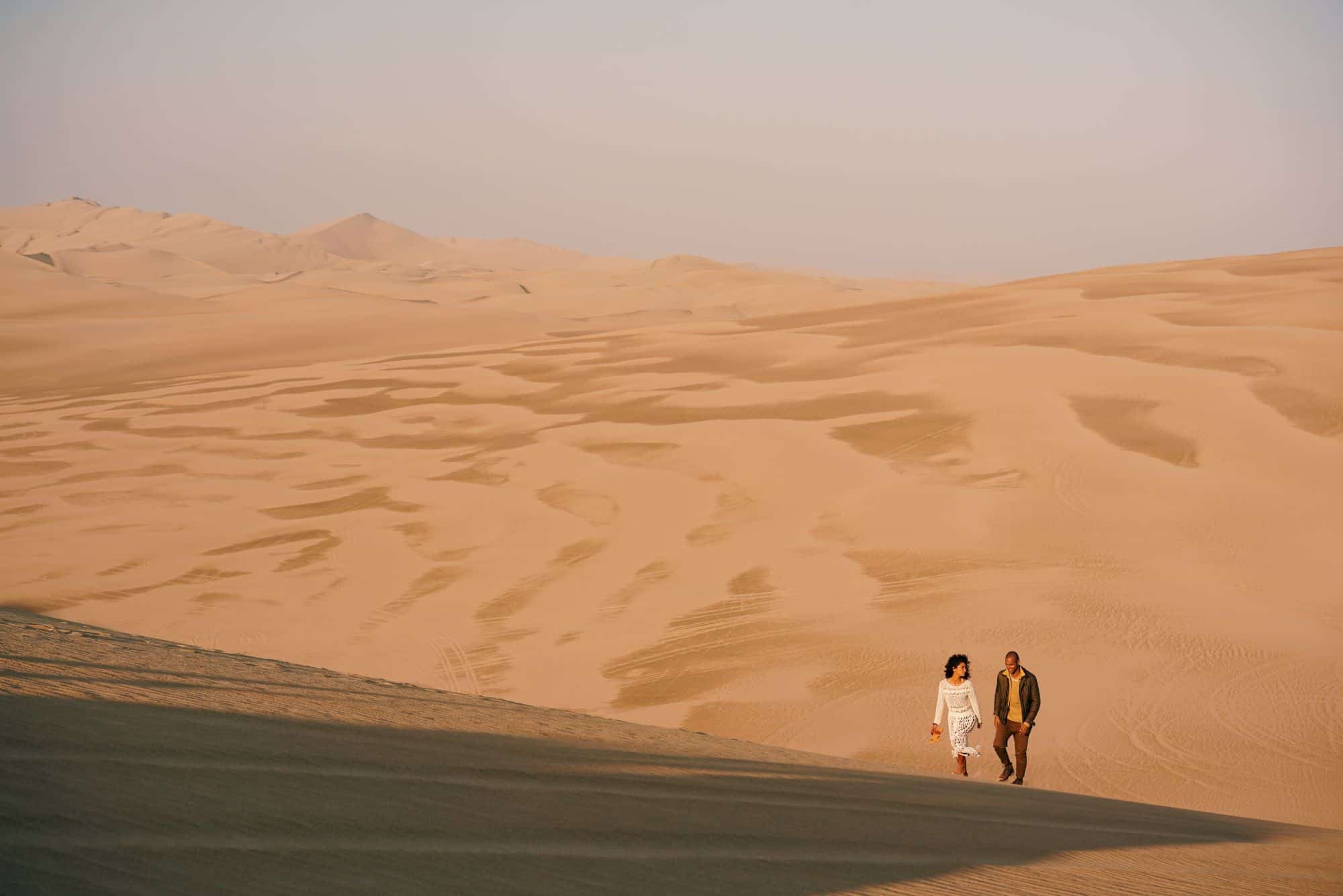A couple walking across desert sand dunes