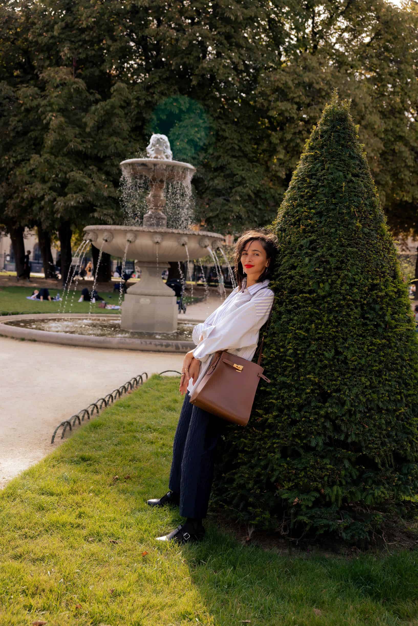 woman leaning against shrub with fountain in background